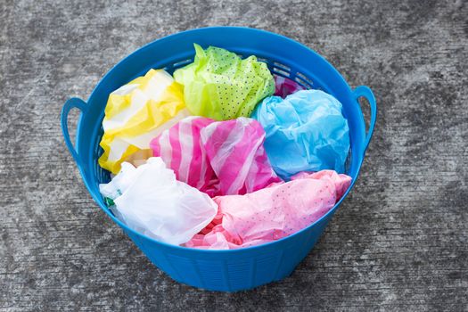 Colorful plastic bags in trash basket on cement floor background