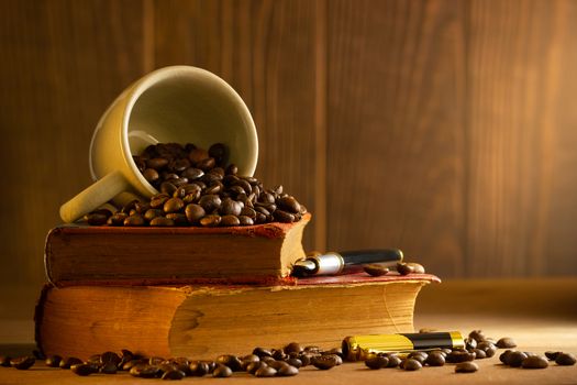 Coffee bean in the white cup and vintage book stacking on wooden table in morning light.