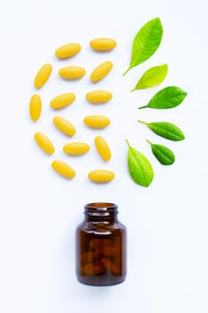 Vitamin C bottle and pills with  green leaves on white background