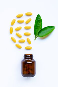 Vitamin C bottle and pills with  green leaves on white background