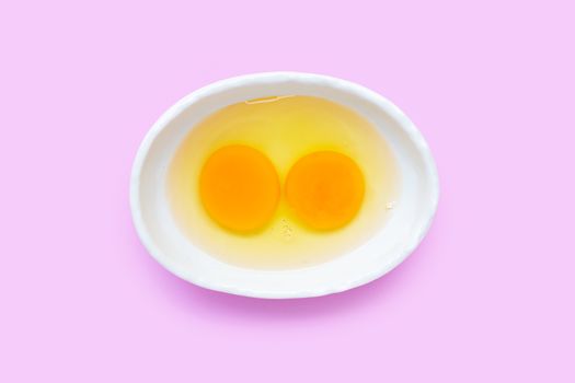 Two egg yolk and white in a bowl on pink background.  Top view