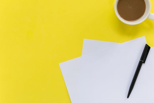 Sheets of white blank paper with pen on yellow background.