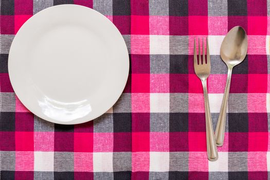Empty plate with spoon and fork on table background.