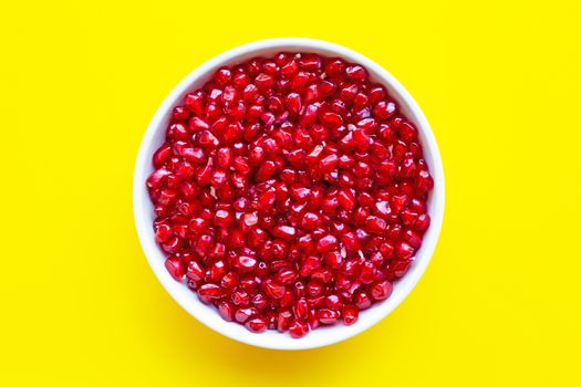 Top view of pomegranate seed in white bowl on yellow background.