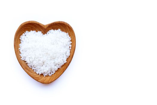 Flower of salt in heart shaped wooden bowl on white background.
