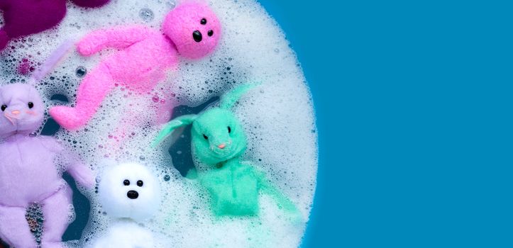 Soaking rabbit dolls with bear toys in laundry detergent water dissolution before washing. Laundry concept, Top view with blue background.
