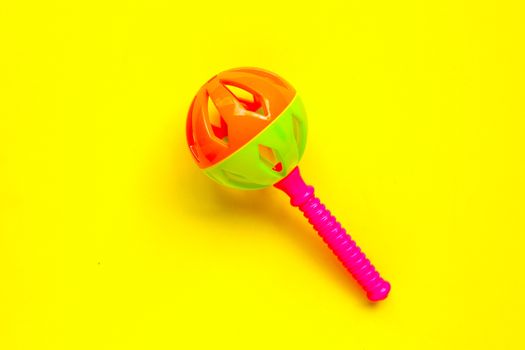 Colorful baby rattle on yellow background.