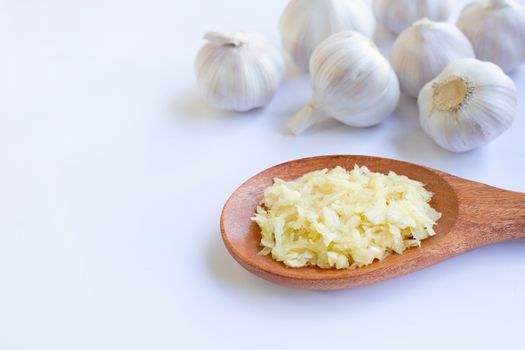 Fresh chopped garlic on wooden spoon with garlic head on white background