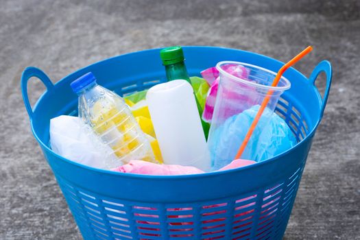 Plastic bottles in blue waste basket on cement floor background.