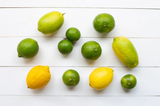 Ripe lemons and limes on white wooden background.
