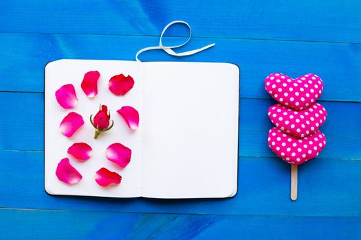Diary notebook with rose and valentine's hearts on blue wooden background. Concept for Valentine's Day