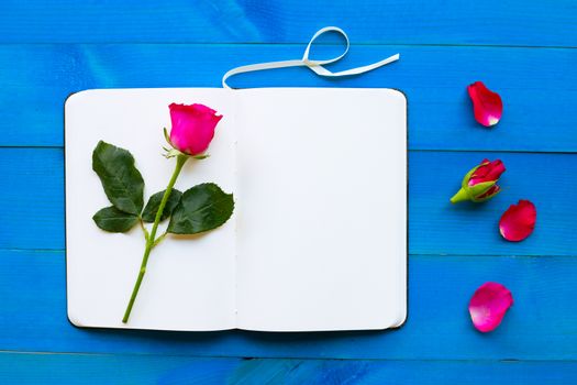 Diary notebook with rose on blue wooden background. Concept for Valentine's Day