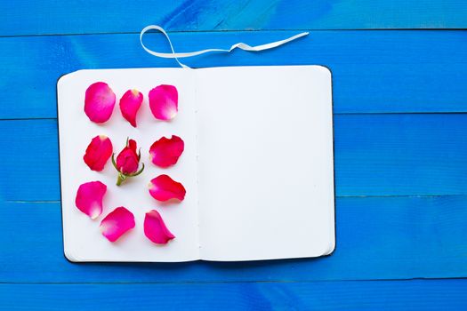 Diary notebook with rose on blue wooden background. Concept for Valentine's Day. 