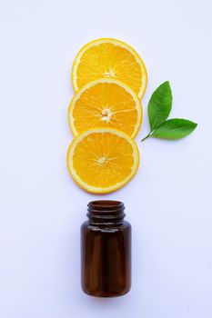Brown medicine glass bottle with orange fruit  slices and green leaves on white background.