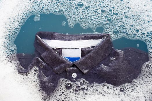 Grey polo shirt soak in powder detergent water dissolution, washing cloth. Laundry concept