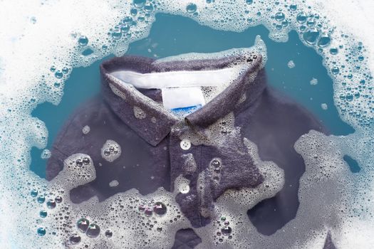 Grey polo shirt soak in powder detergent water dissolution, washing cloth. Laundry concept