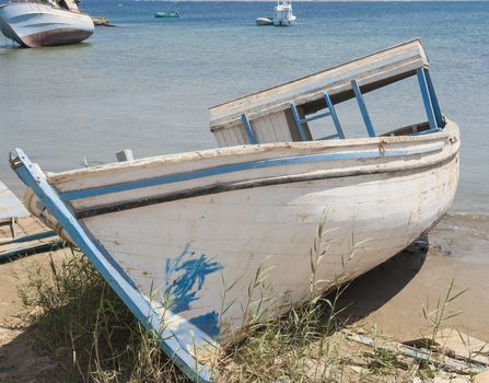 Old derelict small boat abandoned on beach by coast