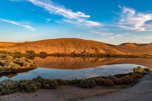 Desert oasis of water with vegetation along with blue sky and clouds at Bruneau Dunes, Idaho.