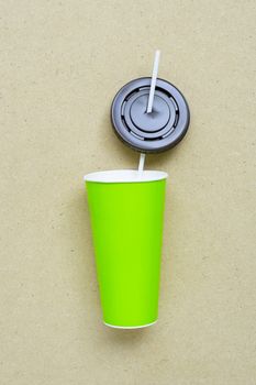 Green paper coffee cup with straw and plastic cap on plywood background.