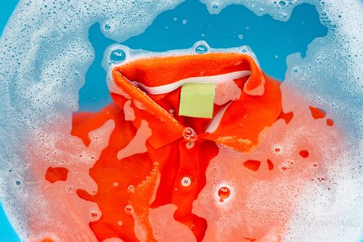 Orange polo shirt soak in powder detergent water dissolution, washing  cloth. Laundry concept