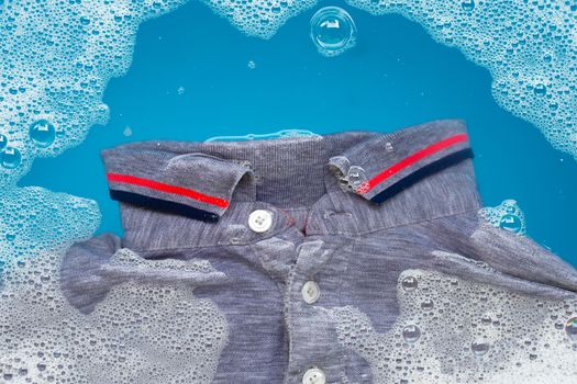 Grey polo shirt soak in powder detergent water dissolution, washing cloth. Laundry concept