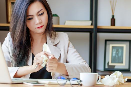 Asian businesswoman squeeze paper in hand sitting at office desk covered with crumpled paper, feeling tired after work fail, give up, no idea