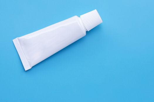 Small white toothpaste tube on blue background. Copy space