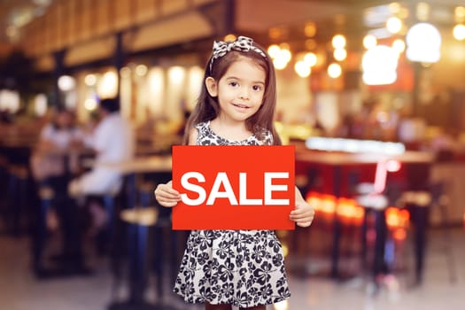 sale discount promotion for shop concept : adorable girl holding red sign with text sale in white color in front of shop , restaurant or cafe
