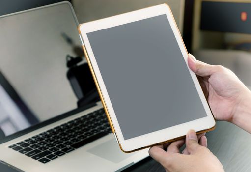 Business man hand holding a white tablet with blank screen in office.