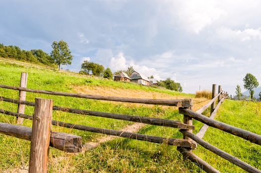 A wooden fence, a farm and a field in the Ukrainian Carpathian Mountains, under a cloudy sky