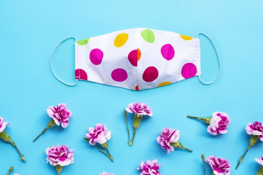 Handmade colorful cloth mask with carnation flower on blue background. Top view