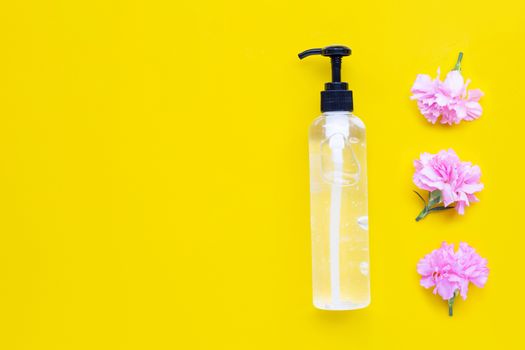 Alcohol hand sanitizer gel in pump bottle with pink carnation flower on yellow background. Hand hygiene corona virus protection concept.