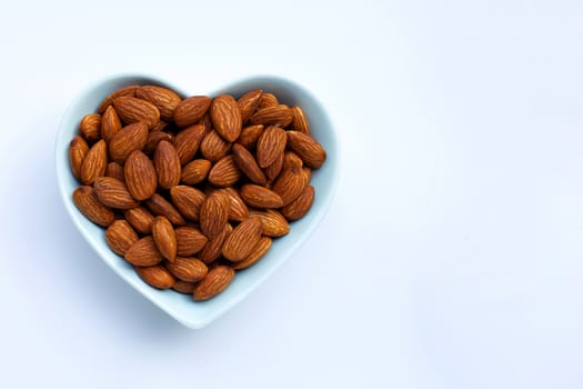 Almonds in heart shape bowl on white background. Copy space