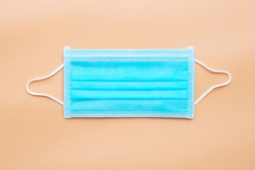 Protective medical mask with rubber ear straps on cream color background. Top view