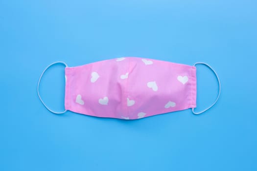 Handmade pink cloth with white hearts mask on blue background. Top view