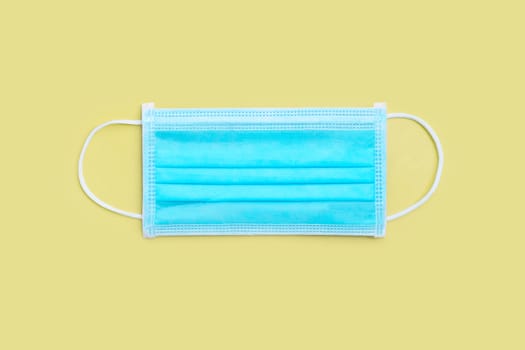 Protective medical mask on yellow background. Top view