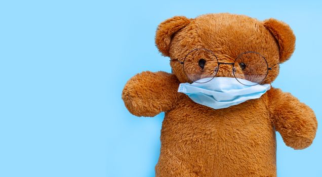 Teddy bear with mask on blue background. Copy space