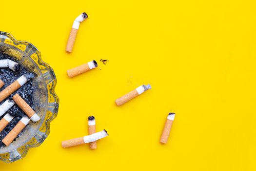 Ashtray and cigarettes on yellow background. Copy space