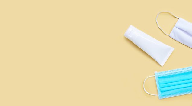 Masks and Alcohol hand sanitizer gel in white glossy plastic tube for hygiene corona virus (Covid-19) protection. Yellow background with copy space