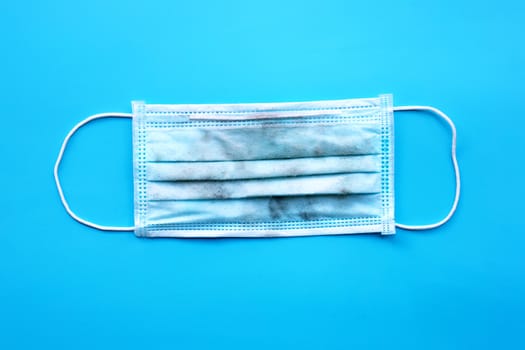 Dirty surgical mask on blue background. Top view