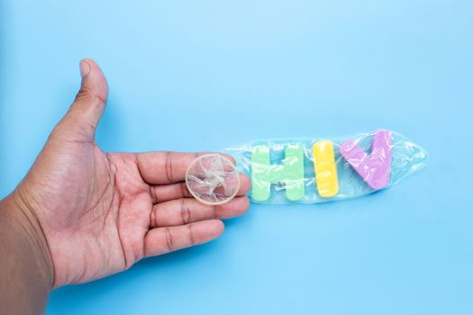 Hand with  "HIV" colorful alphabet in condom on blue background. Save sex concept, Topv view
