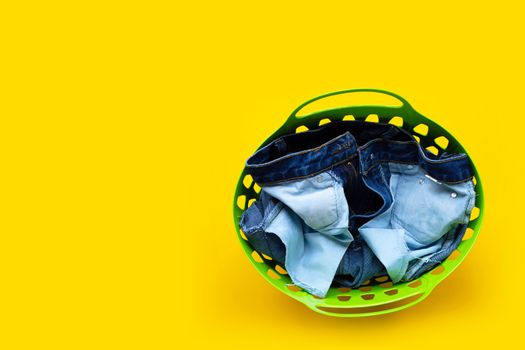 Jeans in green laundry basket on yellow background. Copy space