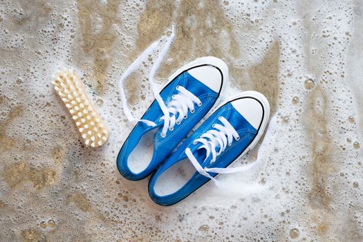 Sneakers with foam of powder detergent water dissolution and wooden brush on cement floor. Washing dirty shoes. Top view