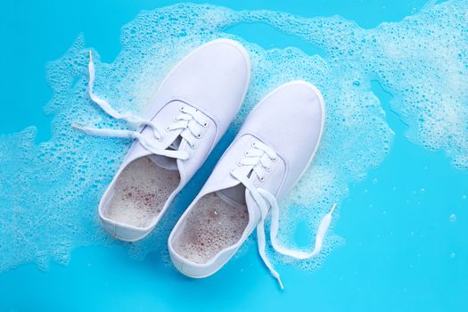 Sneakers with foam of powder detergent water dissolution on blue background. Washing dirty shoes.