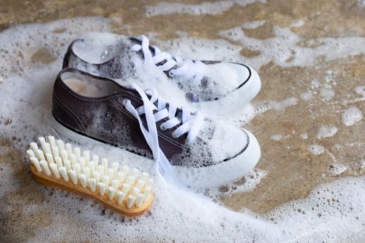 Sneakers with foam of powder detergent water dissolution and wooden brush on cement floor. Washing dirty shoes.
