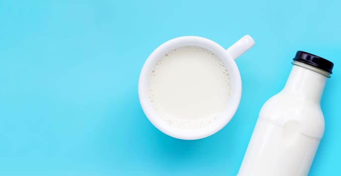 Cup of milk and bottle on blue background. Copy space