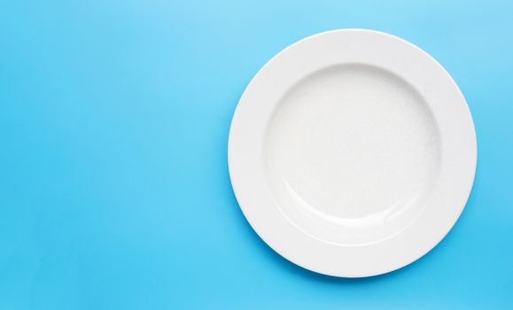 Empty white ceramic plate on blue background. Copy space
