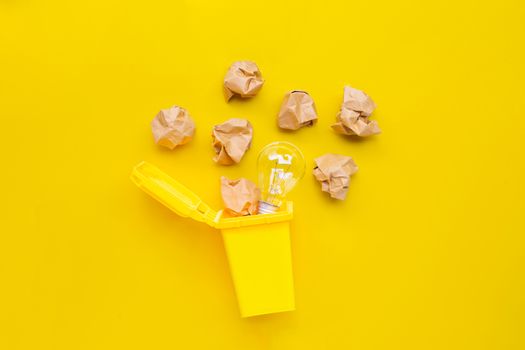 Yellow bin with light bulb and brown crumpled paper on yellow background. Ideas and creative thinking concept. Top view