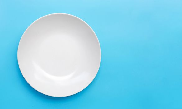Empty white ceramic plate on blue background. Copy space