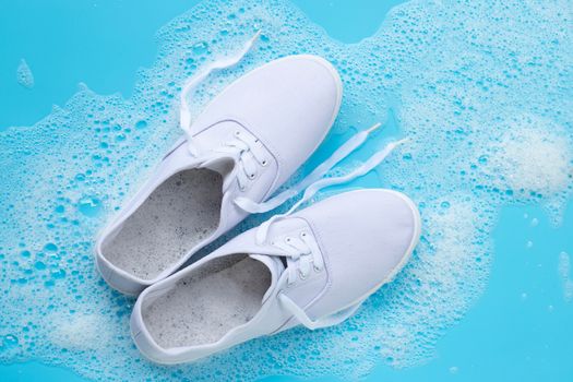 Sneakers with foam of powder detergent water dissolution on blue background. Washing dirty shoes. Top view